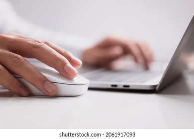 Male hand holds a computer mouse and typing laptop keyboard.