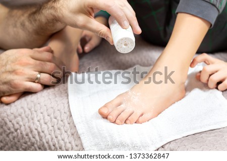 Male hand holds the container with the powder and pour the white powder on child's feet. Medicine against sweating of the feet.