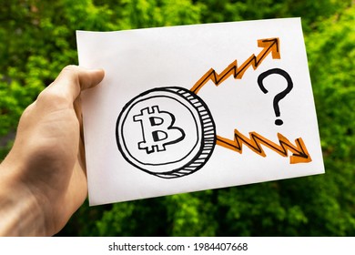 Male Hand Holds The Drawing With Bitcoin Coin, Question Mark And Arrows Leading Up And Down. Rise In Price Or The Process Of Cheapening Of Bitcoin Cryptocurrency In The Future 
