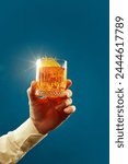 Male hand holds glass of whiskey, rum decorated with slice of citrus and rosemary against blue background. Concept of alcohol, drink, party, degustation, holiday. Copy space for ad