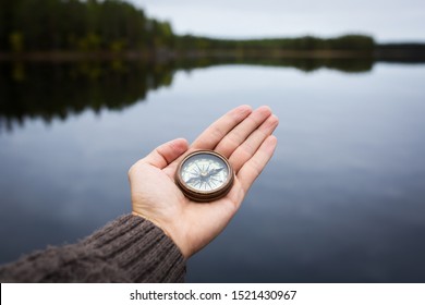 Male hand holds a magnetic compass against the background of the forest and a lake. The concept of finding yourself the way and the truth. - Shutterstock ID 1521430967