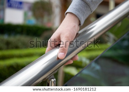 male hand holds metal handrail in a public place
