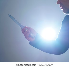 Male Hand Holds Military Knife Isolated On Blue  Background. Backlit. 