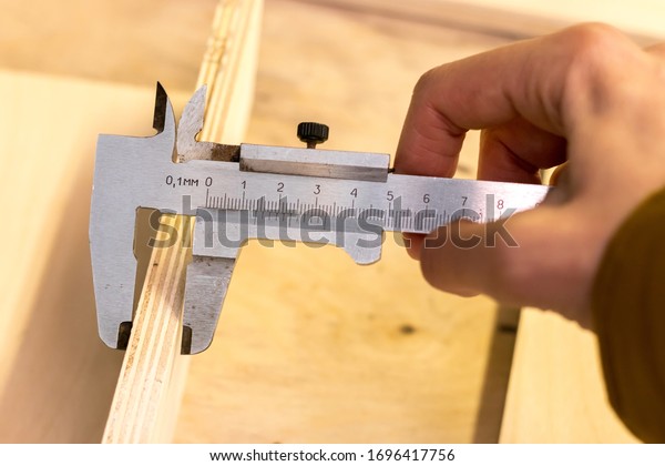 male hand holds an old mechanical\
vernier caliper, measures the thickness of\
plywood