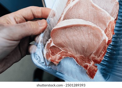 A male hand holds packaged pork meat in plastic packaging, preparing to cook a French meal for lunch or dinner at home, emphasizing freshness and readiness - Powered by Shutterstock