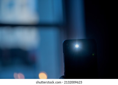  Male hand holds a smartphone with a burning flashlight with lighting window on the background. 