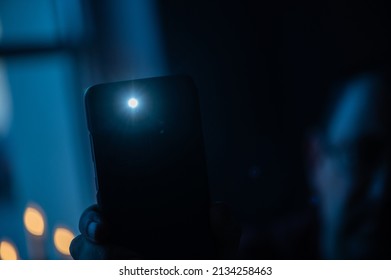 Male hand holds a smartphone with a burning flashlight with lighting window on the background.