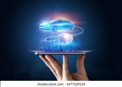 A male hand holds a smartphone with a hologram of an electric vehicle with a charging wire. The concept of electromobility, e-motion, green transport, modern technology