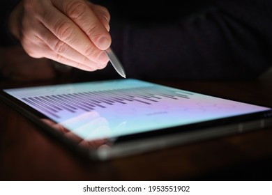 Male Hand Holds Stylus Over Screen Of Tablet With Commercial Charts In Dark