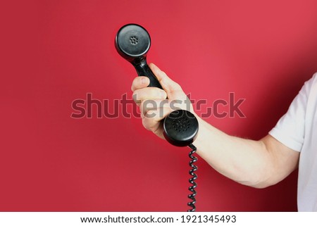 male hand holds a telephone receiver Handset from vintage apparatus on red background, concept of anonymous psychological assistance, helpline number, modern communication technology, call center