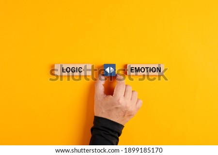 Male hand holds a wooden cube with arrow icon between the options of logic or emotion. Emotional or logical decision making concept.

