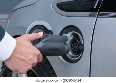 Male hand inserts or unplugs the electric vehicle and close the lid. Electric vehicle charging technology concept. Businessman holds the charging plug wire from the hybrid car