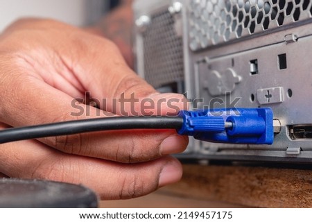 male hand installing VGA cable in a computer server cpu case on a wooden table in a room.