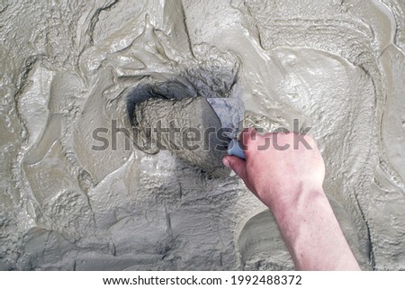 Male hand kneading cement mortar with a trowel, close-up. Construction works.