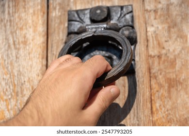 Male hand knocking with an old black iron knocker on a rustic wooden door. Close-up with selective focus - Powered by Shutterstock