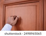 Male hand is knocking on wooden door, conceptual image. Visitor or guest is at the door.