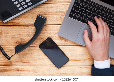 Male Hand, Laptop, IP Phone, Mobile Phone And Notebook On The Wooden Background. Top View. Ip Telephony And Video Meetings For Business Concept. 