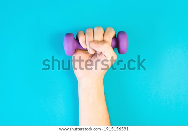 Male hand lifting up dumbbell. Man holding\
sports tool at home on blue\
background.