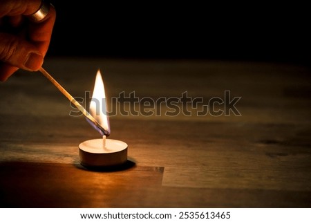 Male hand lighting a small white tea candle on a wooden table, close up shot. Tealight ambiance concept.