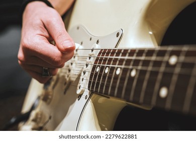 Male hand with long nails playing a white single coil electric guitar with a plectrum, close up, rock blues live music