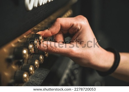 Male hand with long nails turning knob on a guitar amplifier, live music studio recording rock metal session, guitar player musician
