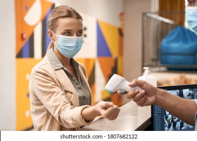 Male Hand Measuring Body Temperature Of A Young Businesswoman Wearing Medical Mask Or Female Office Worker, Temperature Screening At Work