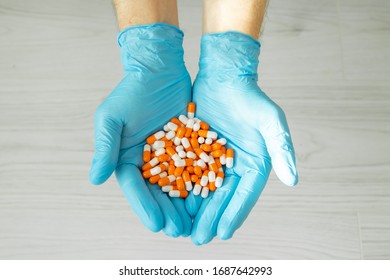 Male Hand In A Medical Glove Holds A Handful Of Orange Pills