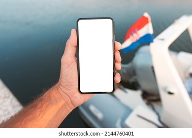 Male Hand With Mobile Smart Phone In Front Of Sailing Boat With Croatian Flag, Blank Mockup Screen, Selective Focus