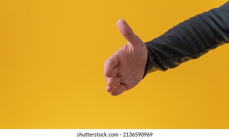 Male hand offering a handshake over yellow background.