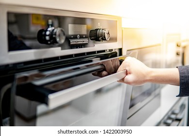 Male hand opening oven door in the kitchen showroom. Buying cooking appliance for domestic kitchen. Home improvement concept