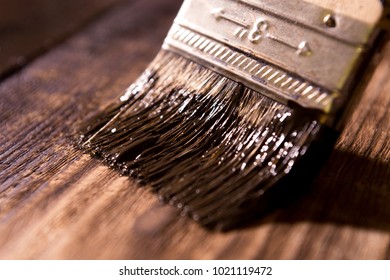 male hand paint wooden surface with brown paint using a paintbrush