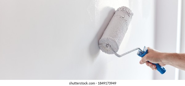 Male hand painting wall with paint roller. Painting apartment, renovating with white color paint