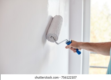 Male hand painting wall with paint roller. Painting apartment, renovating with white color paint