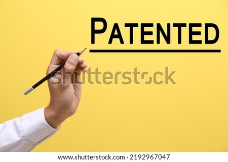 Male hand with pencil and word PATENTED on yellow background