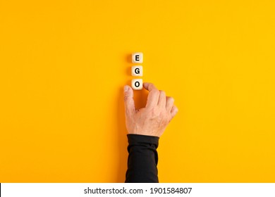 Male hand placing the wooden blocks with the word Ego on yellow background. Personal ego concept.