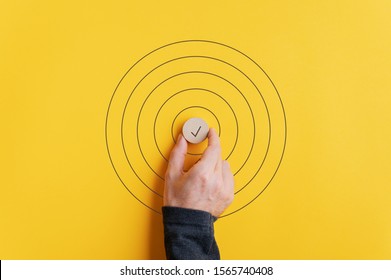 Male hand placing a wooden cut circle with check mark on it in the middle of drawn circles over yellow background.