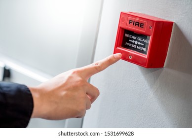 Male Hand Pointing At Red Fire Alarm Switch On Concrete Wall In Office Building. Industrial Fire Warning System Equipment For Emergency.