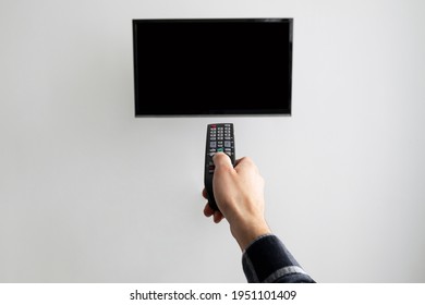 Male Hand Pointing Remote Control At Empty TV Screen On Gray Wall Switching Channels At Home. Unrecognizable Man Watching Television Turning On Plasma Flatscreen TV-Set Indoor. Cropped, Mockup