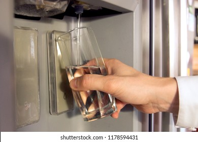 Male Hand Is Pouring Cold Water From Dispenser Of Home Fridge.