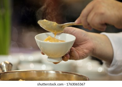 Male Hand Pouring A Spoonful Of Sauce Over Pasta, In A White Dish Bowl.