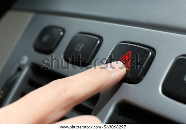Male hand pressing emergency warning button on\
car console, closeup