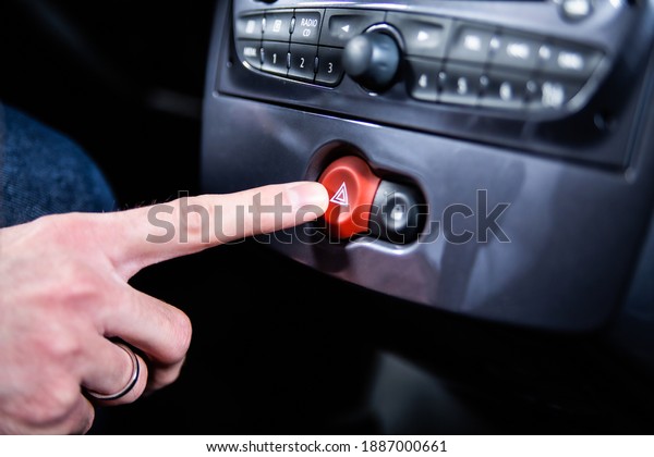 Male hand pressing a hazard warning lights\
button with a red triangle on a car dashboard. A road accident, a\
car breakdown, emergency\
situation.