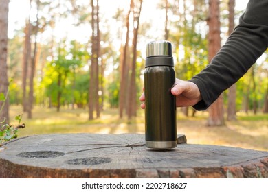 Male hand puts a black thermos bottle on a large tree stump in the forests.