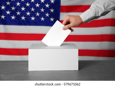 Male hand putting voting ballot into the box  on American flag background