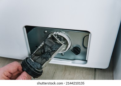 Male hand removes dirty and clogged washing machine pump filter. Repair of household appliances at home with their own hands. the repairman repairs the washing machine