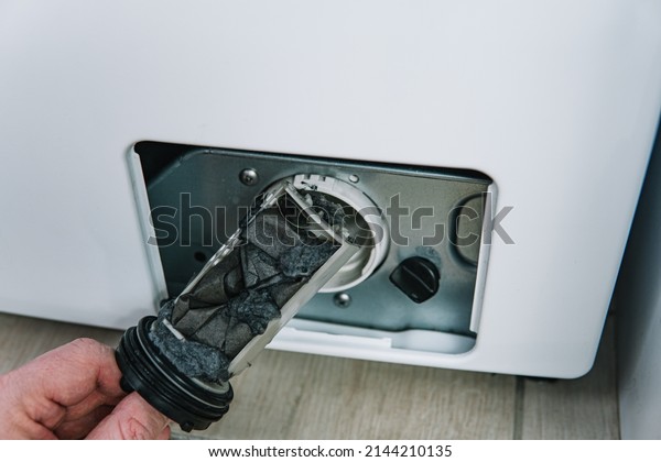 Male hand removes dirty and\
clogged washing machine pump filter. Repair of household appliances\
at home with their own hands. the repairman repairs the washing\
machine