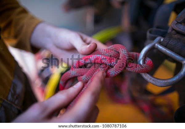 \
The male hand of rope access industry\
worker attaching, tie, secure a red rope with figure of eight knot\
into Aluminium safety harness loop equipment.\
