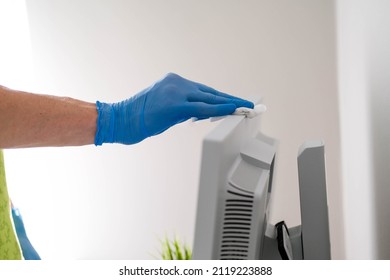 A Male Hand In Rubber Gloves Wipes The Dust From A Computer Monitor With A Napkin. Disinfection At Home, Cleaning In The Context Of The COVID-19 Pandemic.