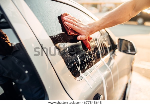 Male hand\
rubbing car window with foam,\
carwash