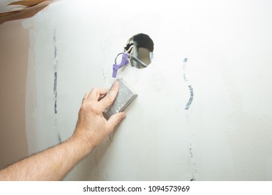 Male Hand Sanding A Patch In A Drywall With Electric Cables Visible Through A Hole